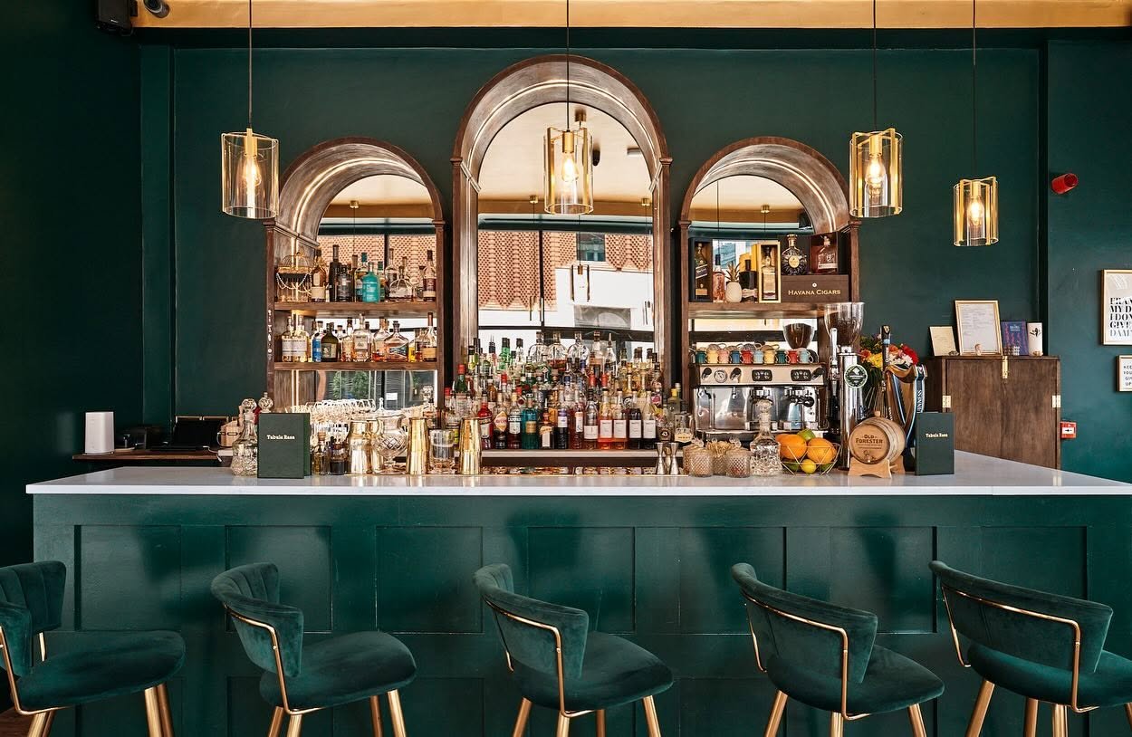 The teal and brass bar at Tabula Rasa, with arched mirrors, hanging lantern lights and green velvet stools