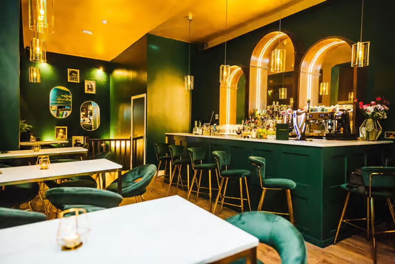 Tabula Rasa's dining room: green velvet booths, marble-top tables and warm brass pendant lighting under a gilded ceiling